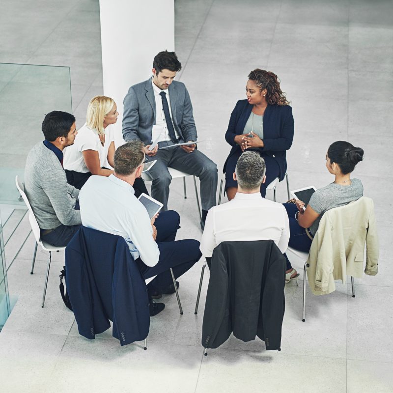 High angle shot of a group of coworkers talking together while sitting in a circle in an office.